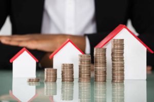 Close-up Of Businesswoman With Different Size Of House Model And Stacked Coins On Desk